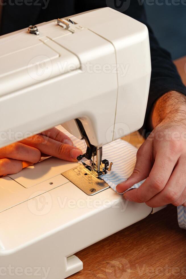 Hands sewing fabric using a sewing machine on a wooden table in a well-lit workspace photo