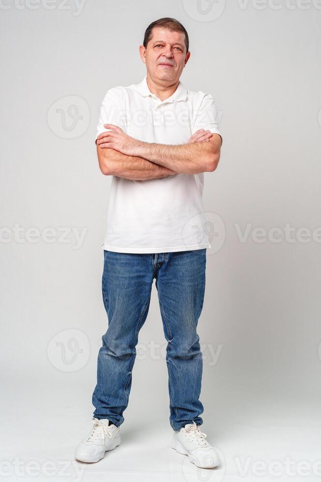 A man poses confidently in a white polo shirt and jeans against a light backdrop photo
