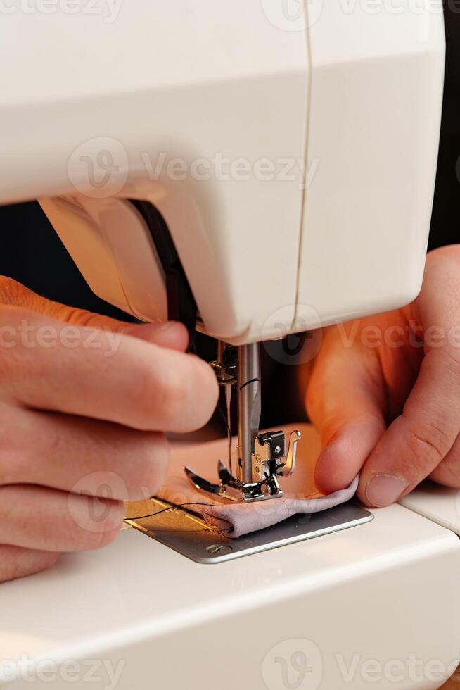 Hands sewing fabric using a sewing machine on a wooden table in a well-lit workspace photo