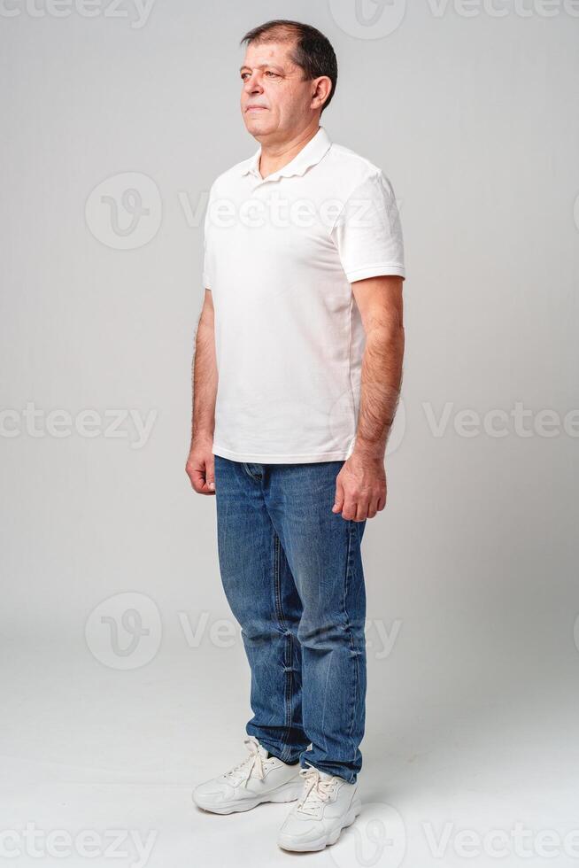 Man standing sideways in casual attire against a plain background photo