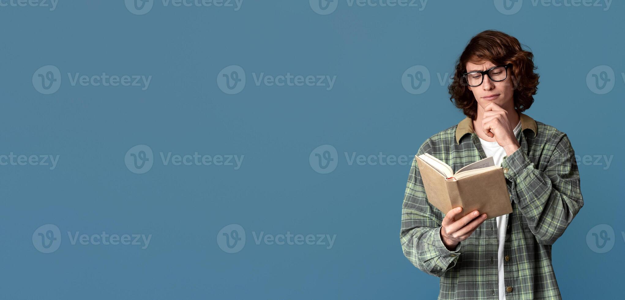 Back to school concept. Industrious student in glasses reading interesting book on turquoise background photo