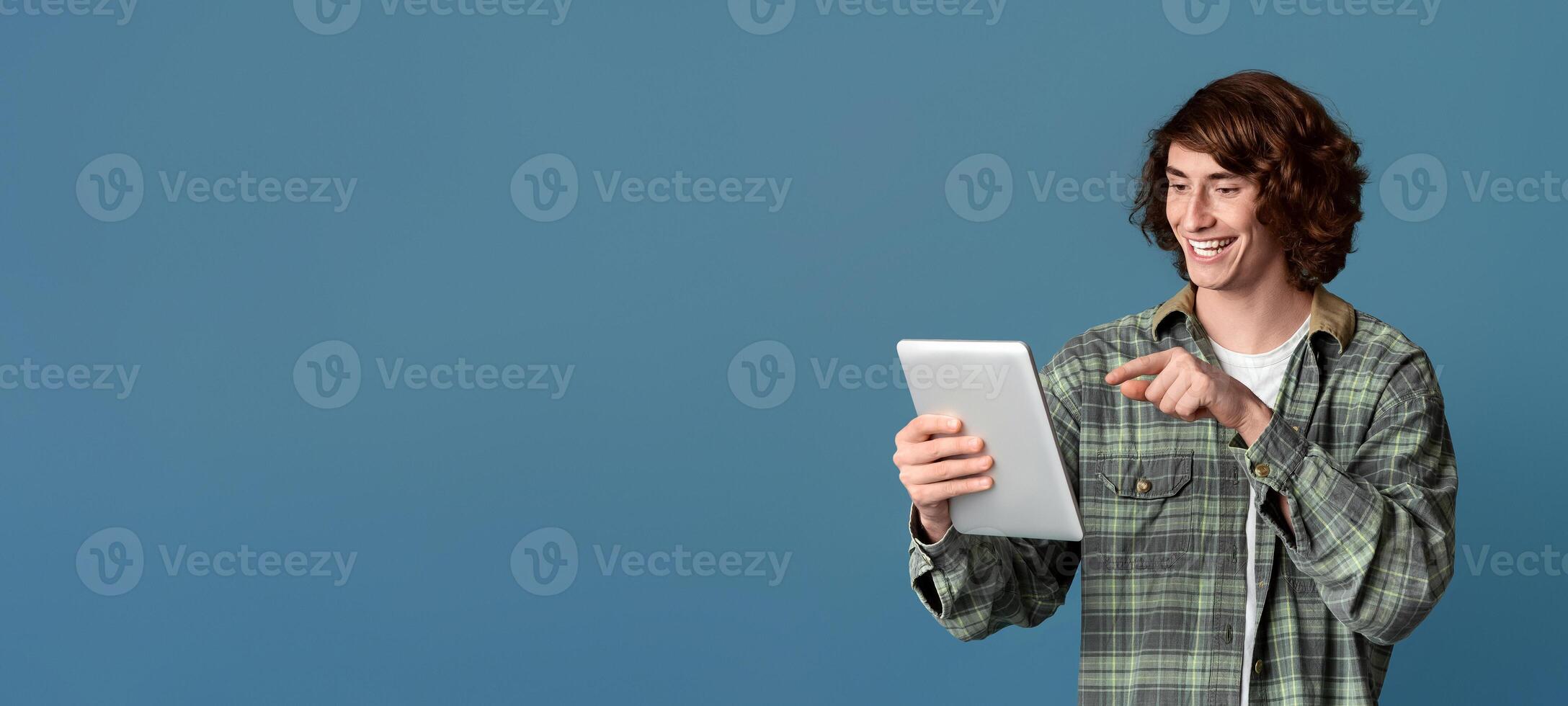 Distance communication. Happy teen guy pointing at tablet computer, chatting online on turquoise background photo