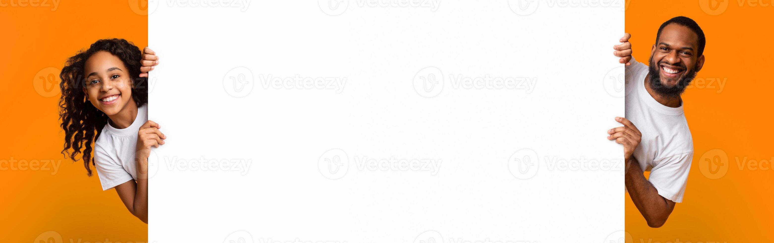 Promotion Billboard Concept. Cheerful African Man Dad And Girl Holding White Advertisement Board, Standing Together On Yellow Background, Looking At Camera Peeping Out The Two Sides Of Sign Board photo