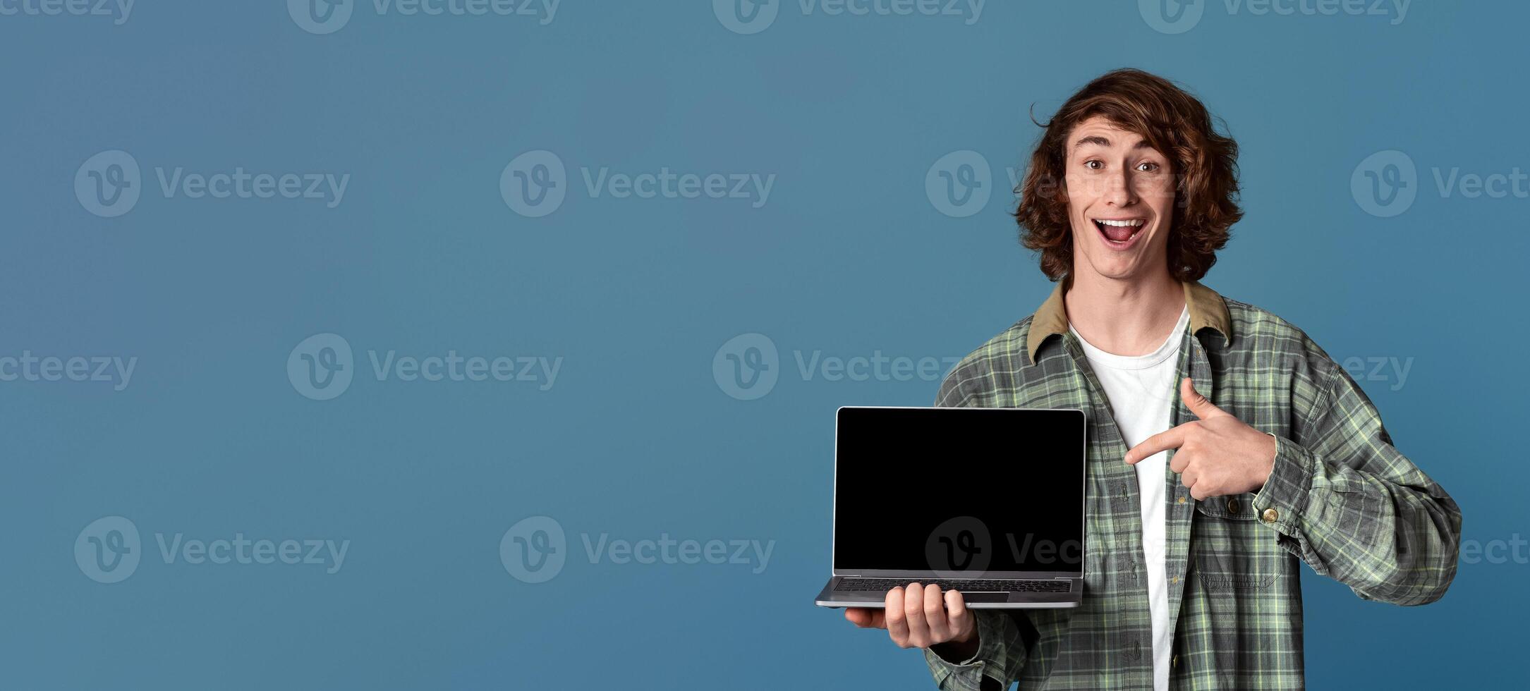 Excited millennial guy pointing at laptop computer with empty screen on turquoise background, space for your ad photo
