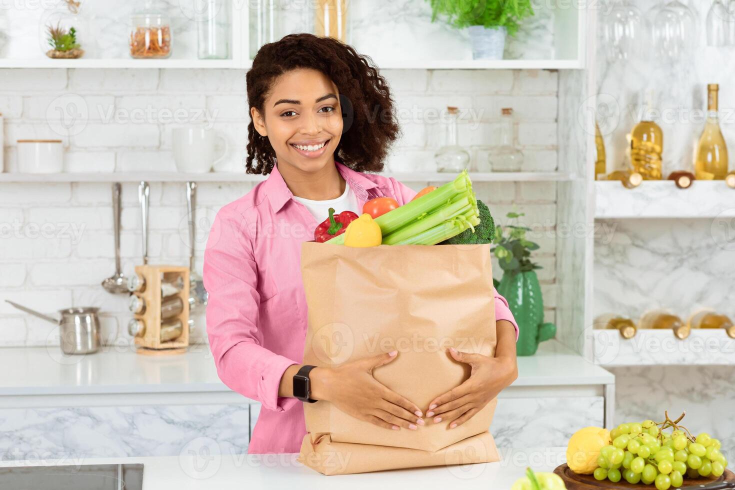 Ready For Quarantine. African woman holding package with fresh food in kitchen, staying at home to prevent infection photo