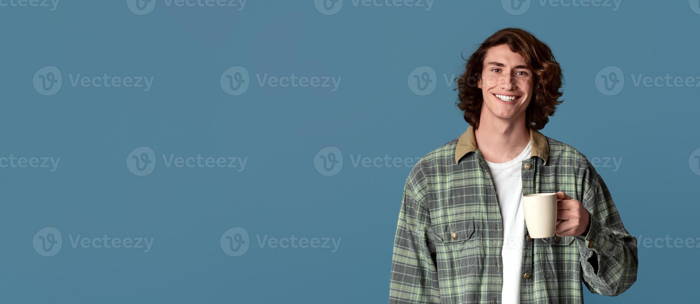 Cool millennial guy holding cup of coffee on color background photo