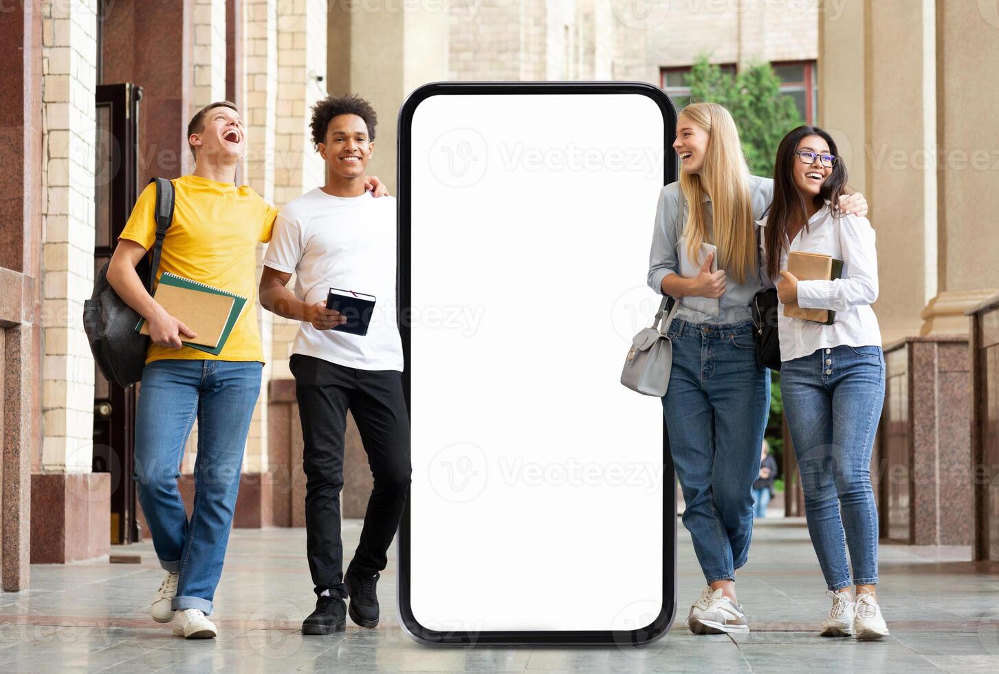 A group of four students enjoys a lighthearted moment outside a university building, passing by huge phone with blank screen photo