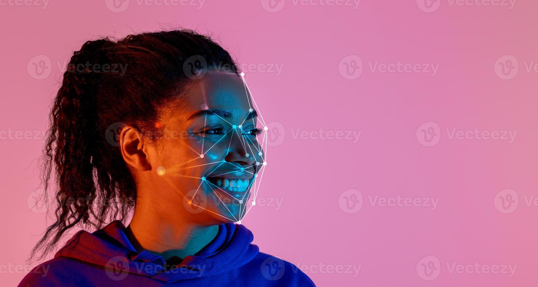 A young black woman smiles against a vibrant pink and blue background while facial recognition markers are visualized over her face, highlighting technology's interaction with human expression. photo
