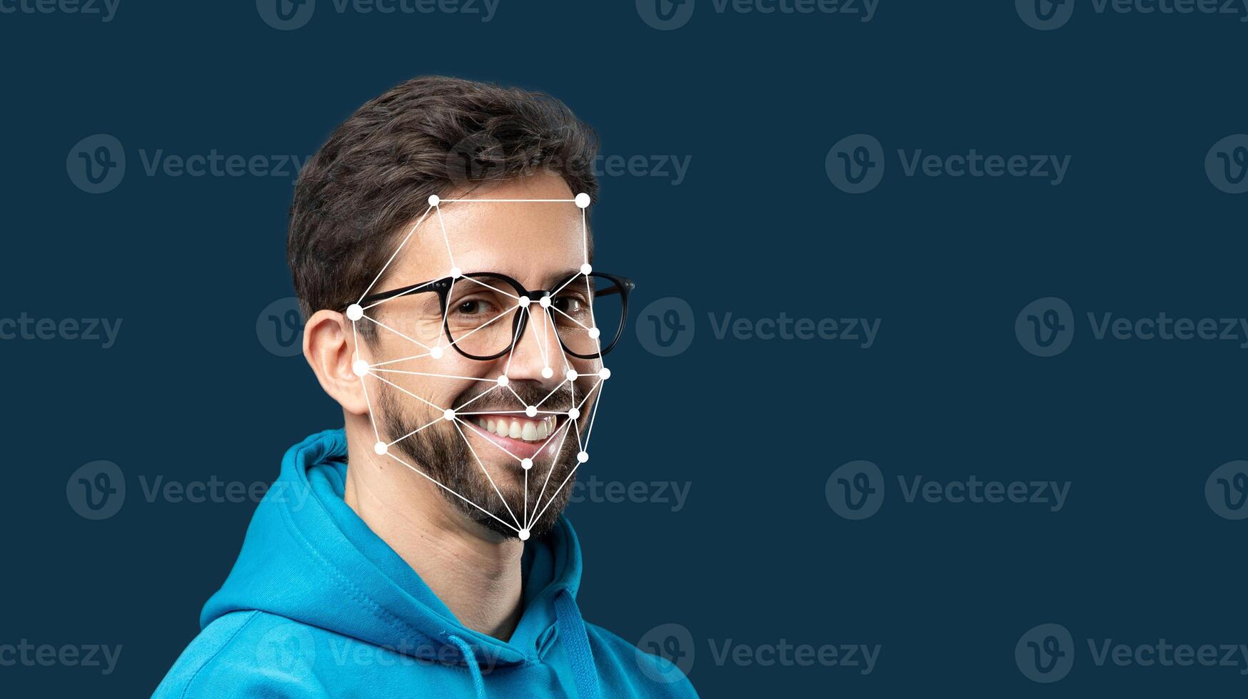 A man wearing glasses and a blue hoodie smiles brightly while facial recognition markers are overlaid on his face, highlighting facial features in a digital context. photo
