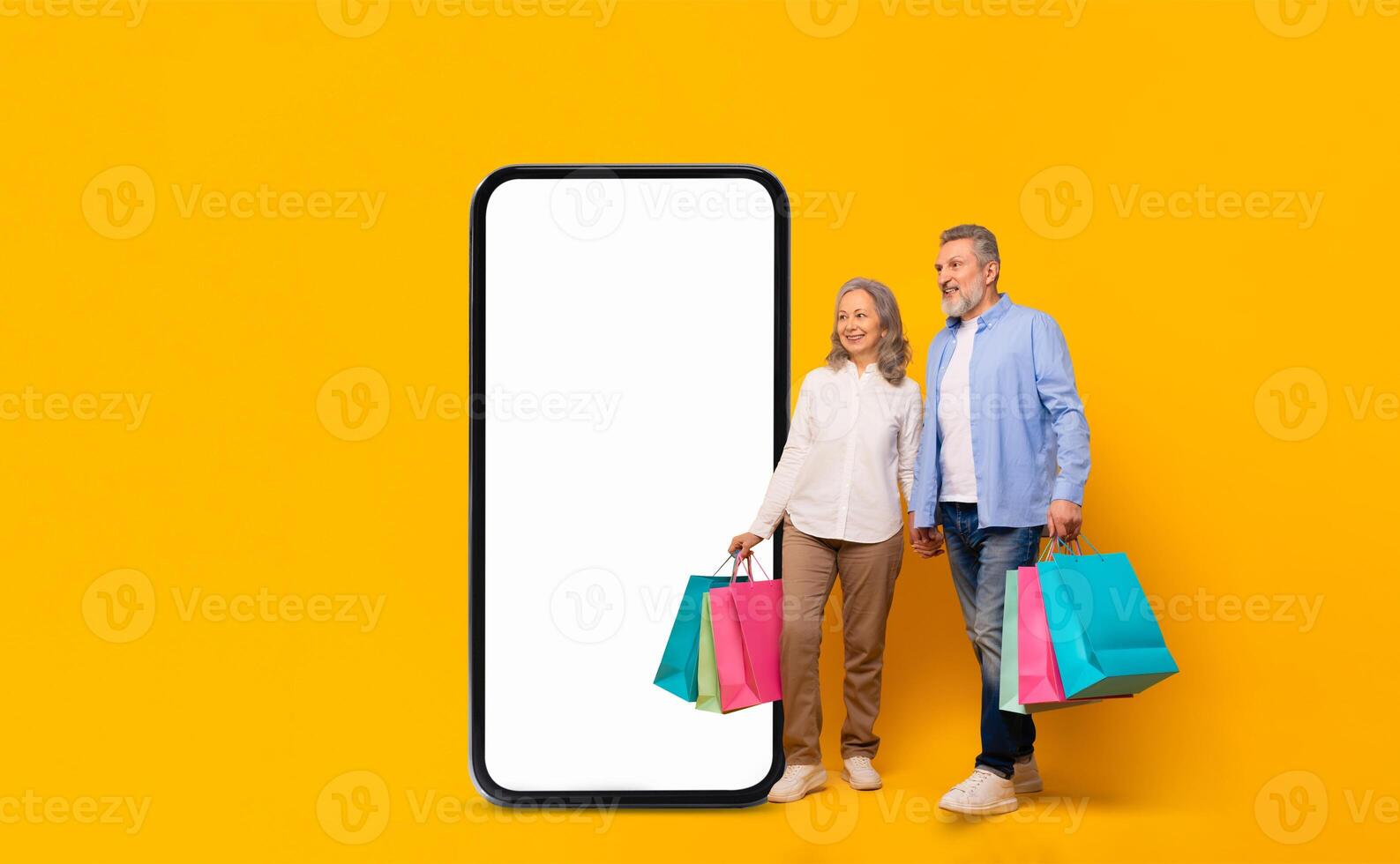A cheerful older couple stands side by side, holding shopping bags in vibrant colors. They are positioned next to a large blank smartphone screen, set against a lively yellow backdrop. photo