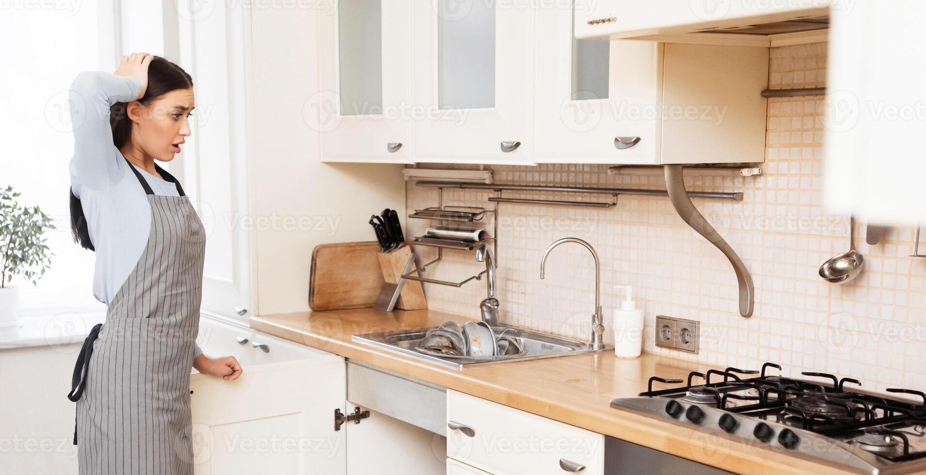 Cleaning Again. Tired and stressed young woman standing at kitchen room, looking at furniture photo