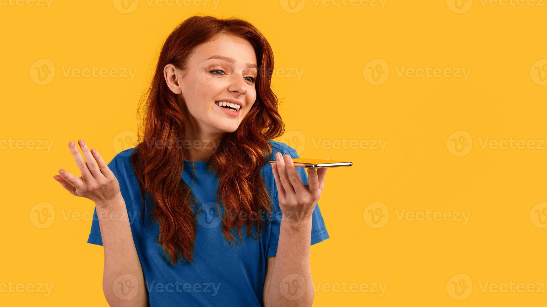 Millennial Girl Using Smartphone Voice Assistant Mobile App Standing Over Yellow Studio Background. Panorama, Copy Space photo