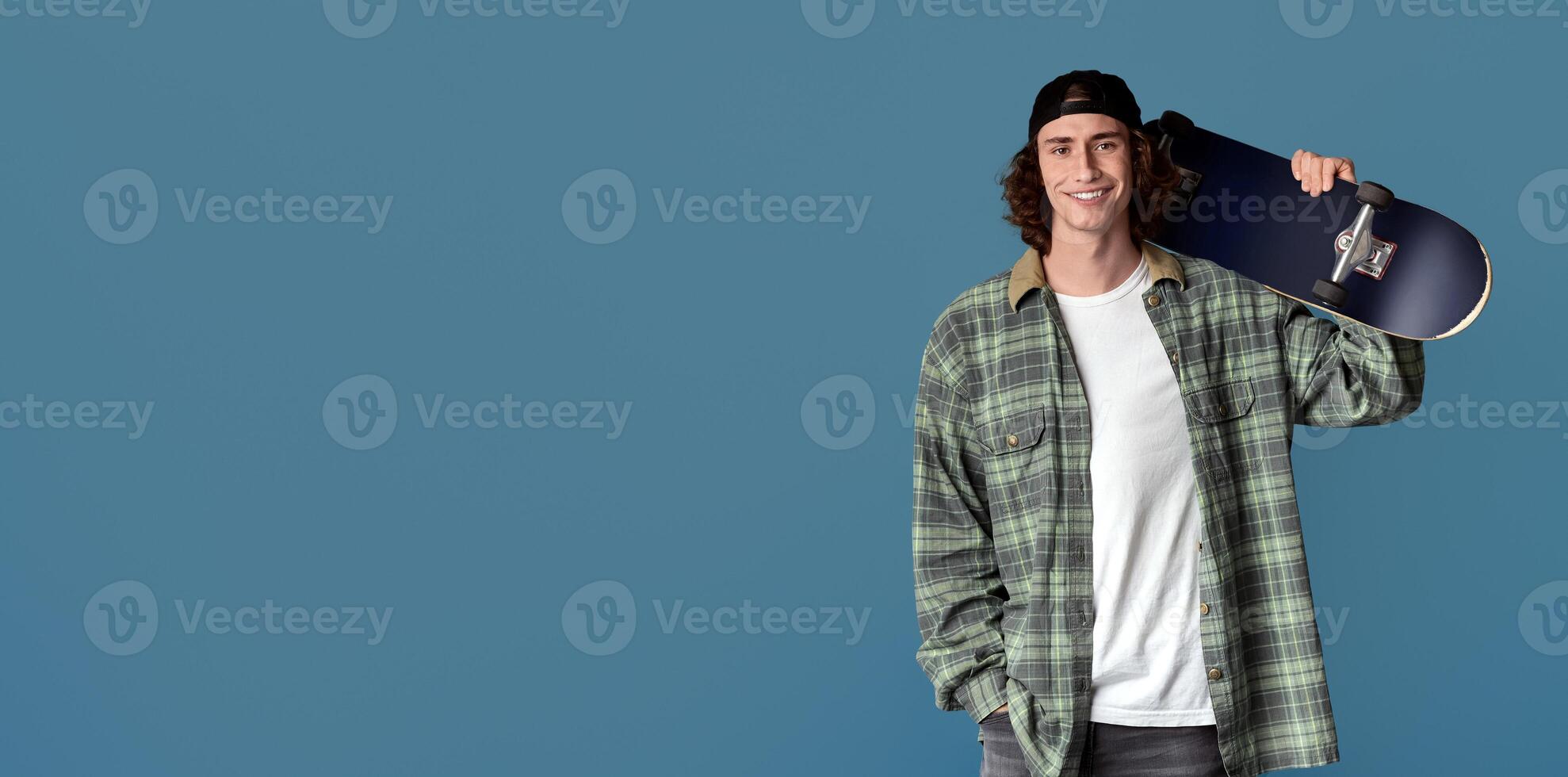 Teenage outdoor activities. Happy young guy holding skateboard on color background photo