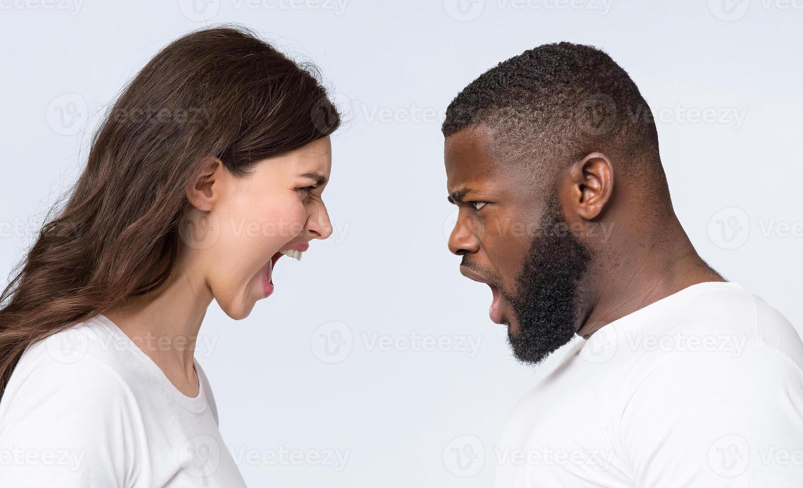 Interracial couples problems. Young man and woman yelling at each other, arguing, having relationship crisis, posing over light background, side view photo