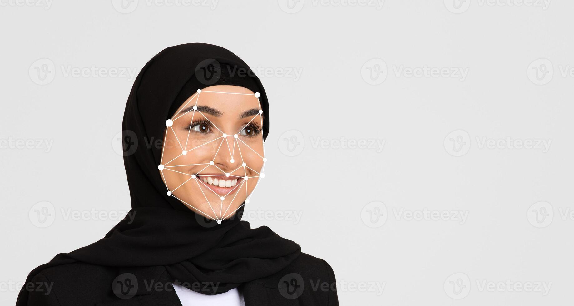 A woman wearing a black hijab smiles while participating in a technology event, where facial recognition technology is demonstrated. The setting highlights advancements in digital innovation. photo