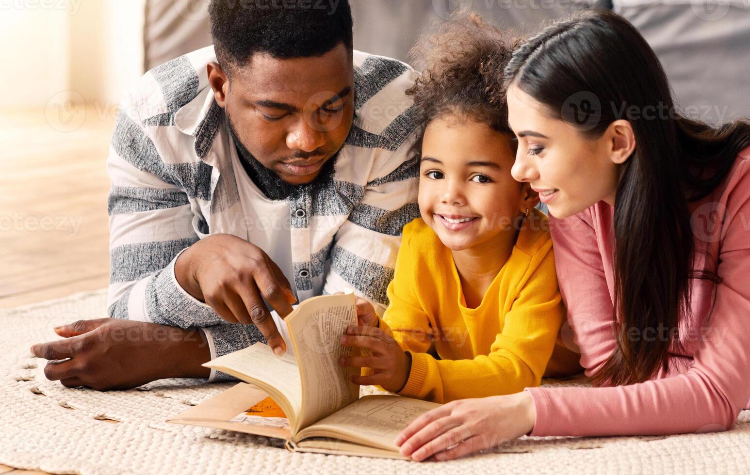 Daughter looks at camera, when her multiracial parents teach her to read at home during covid-19 quarantine photo
