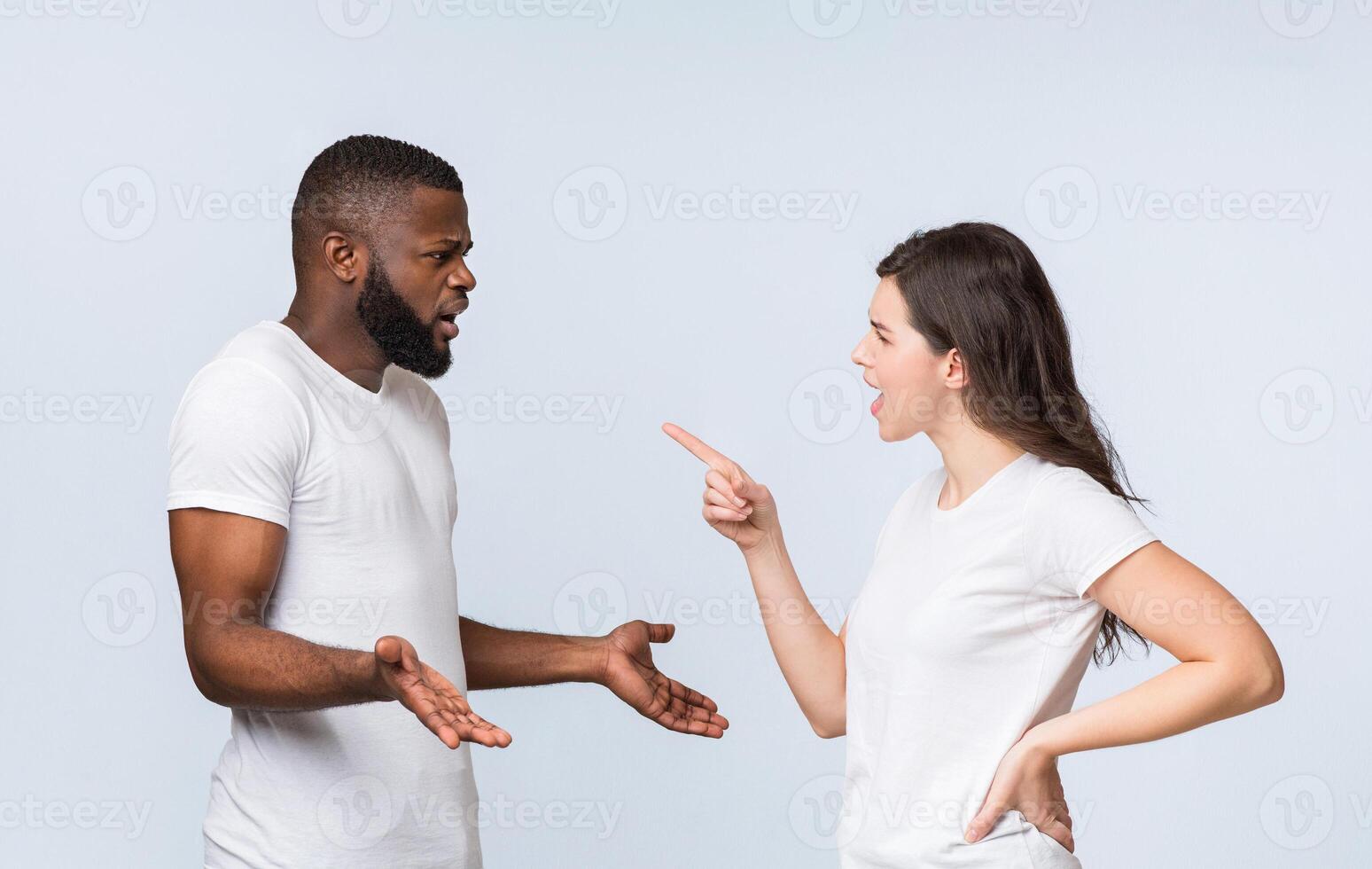 Interracial couple arguing, angry young woman blaming her afro boyfriend, standing together over light background with free space photo