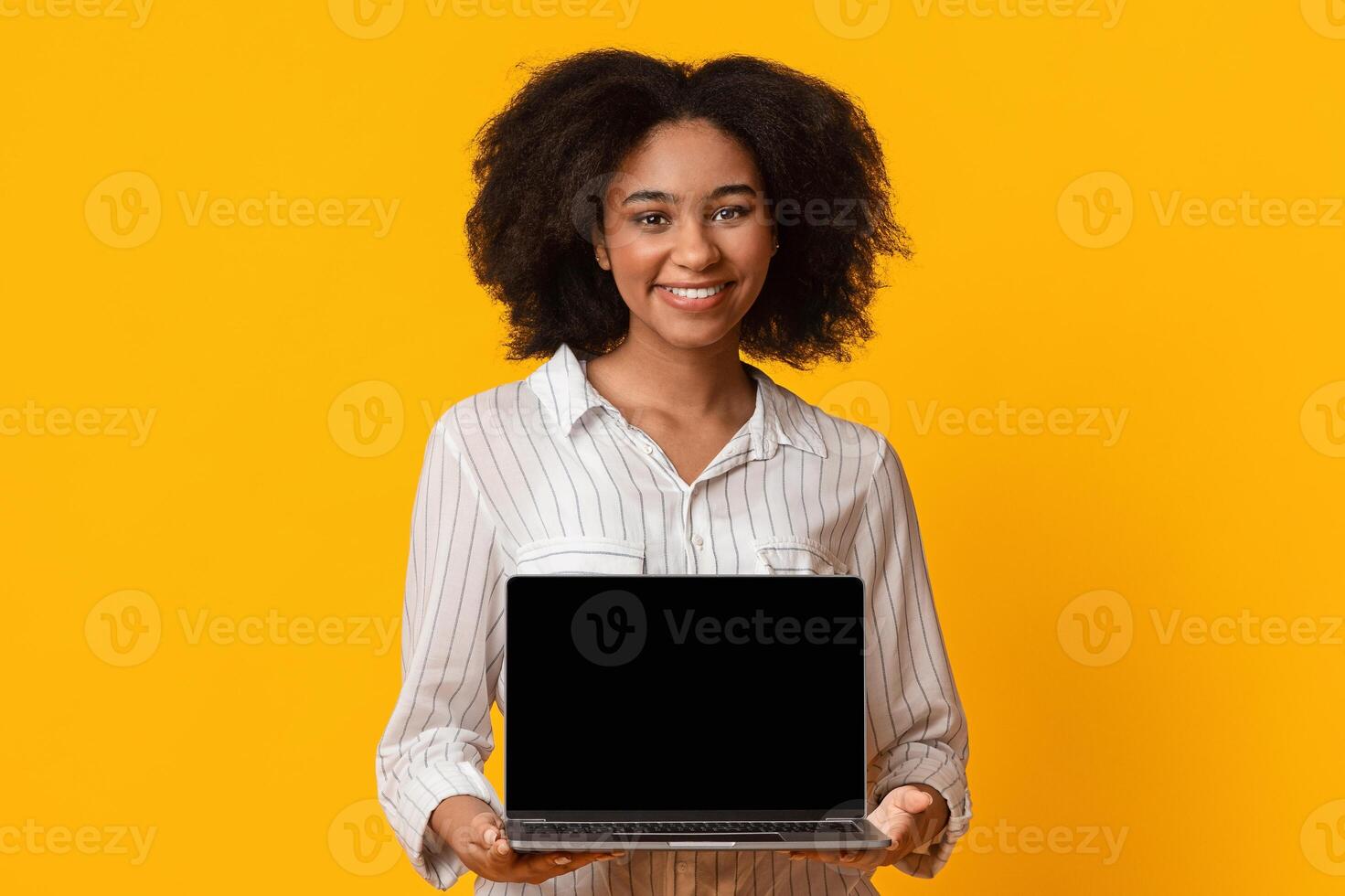 Useful Website. Young black woman demonstrating laptop computer with blank black screen, standing over yellow studio background, mockup, free space photo