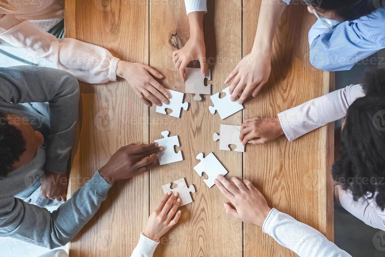Collaboration concept, top view of creative multiracial team sitting around table and putting together puzzle pieces, cropped photo
