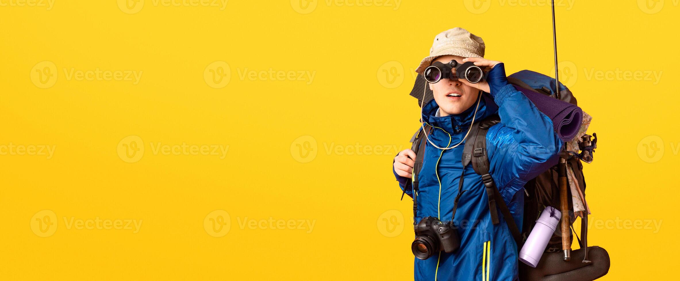 Excited male backpacker looking towards camera through binoculars over orange photo