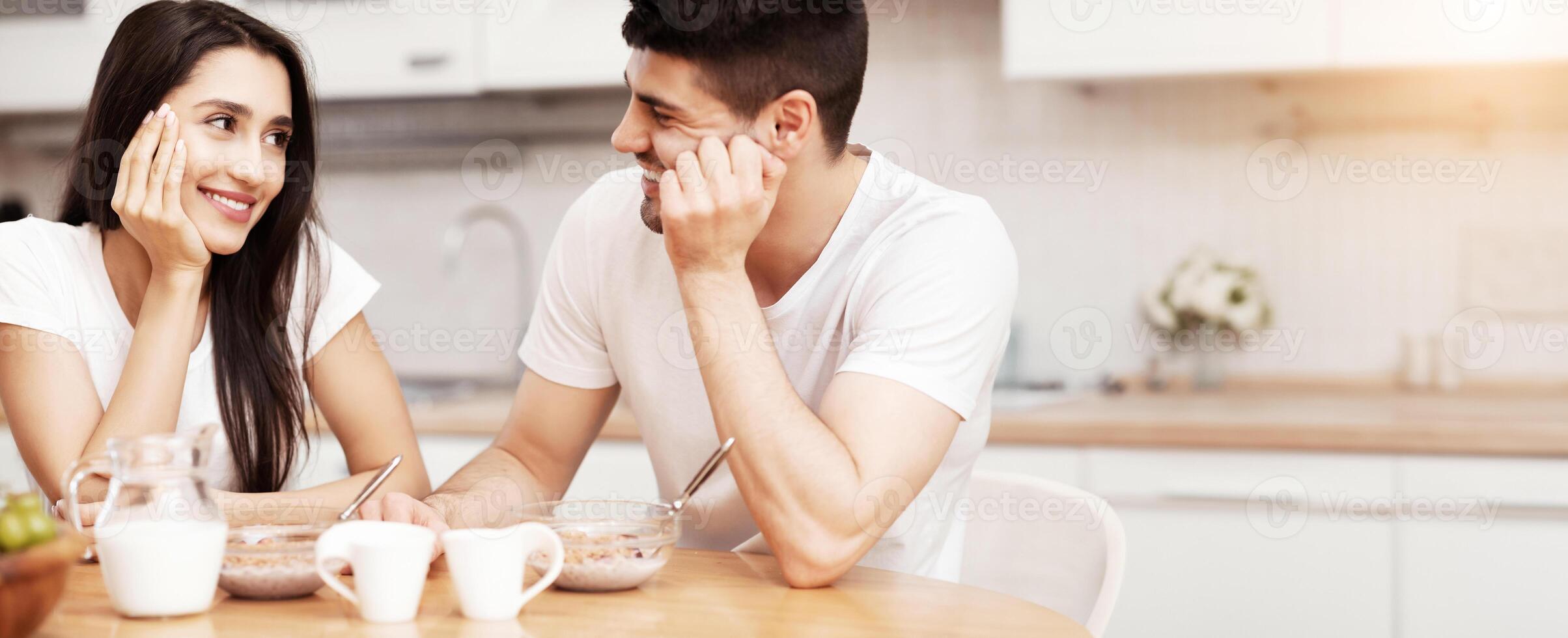 Lovely Family Concept. Portrait of couple sitting at table in modern kitchen and looking at each other photo