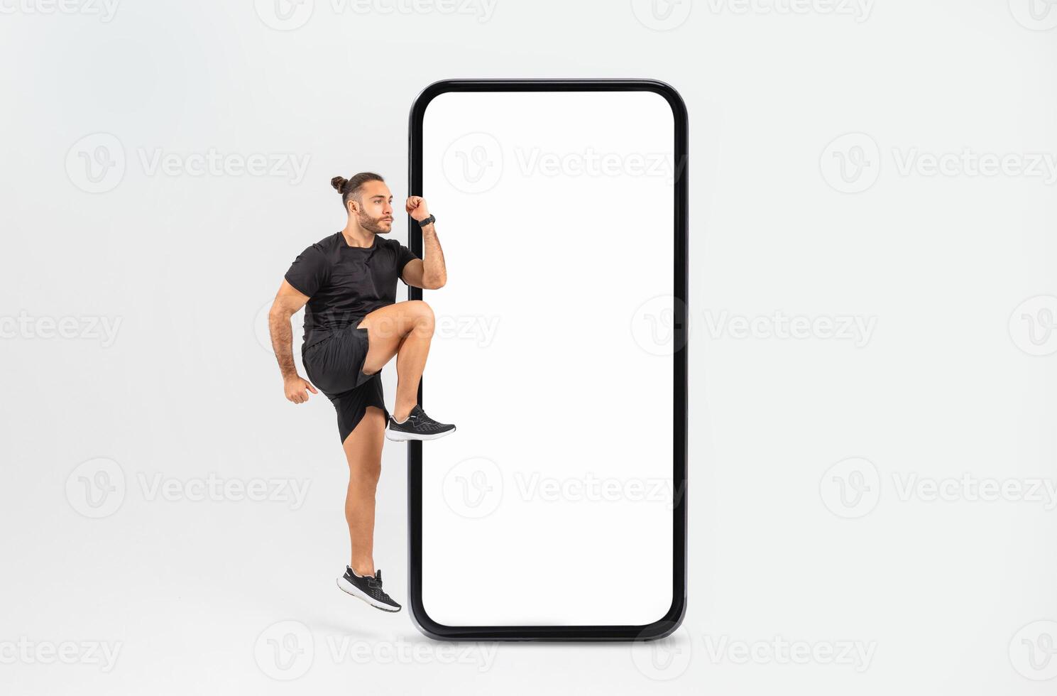 A man is playfully stepping up against a large blank smartphone display, showcasing an energetic pose. The indoor environment is simple and bright, emphasizing his enthusiasm. photo
