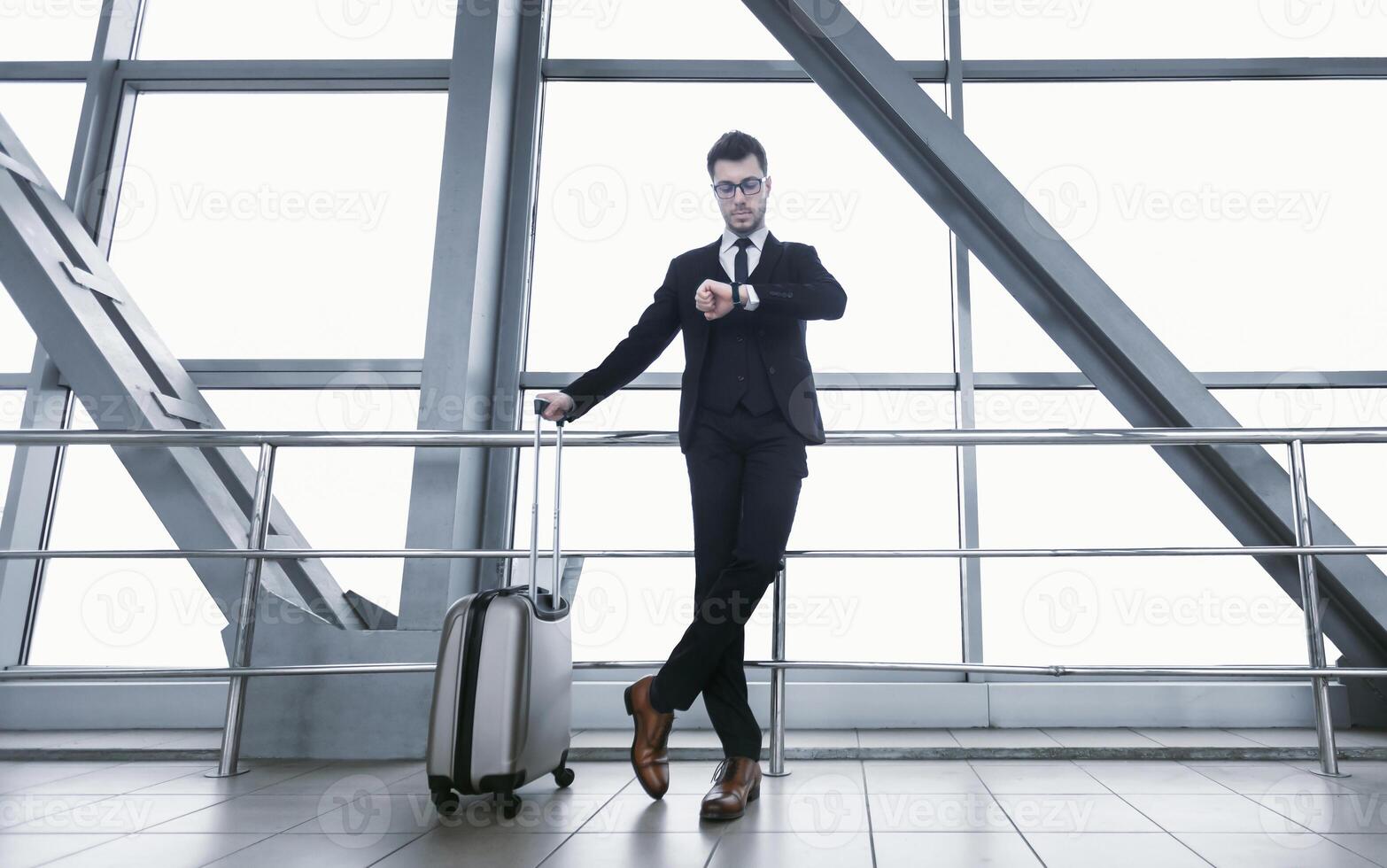 Business Travel. Confident Manager In Specs With Suitcase Checking Time Looking At Wristwatch Standing At Airport photo