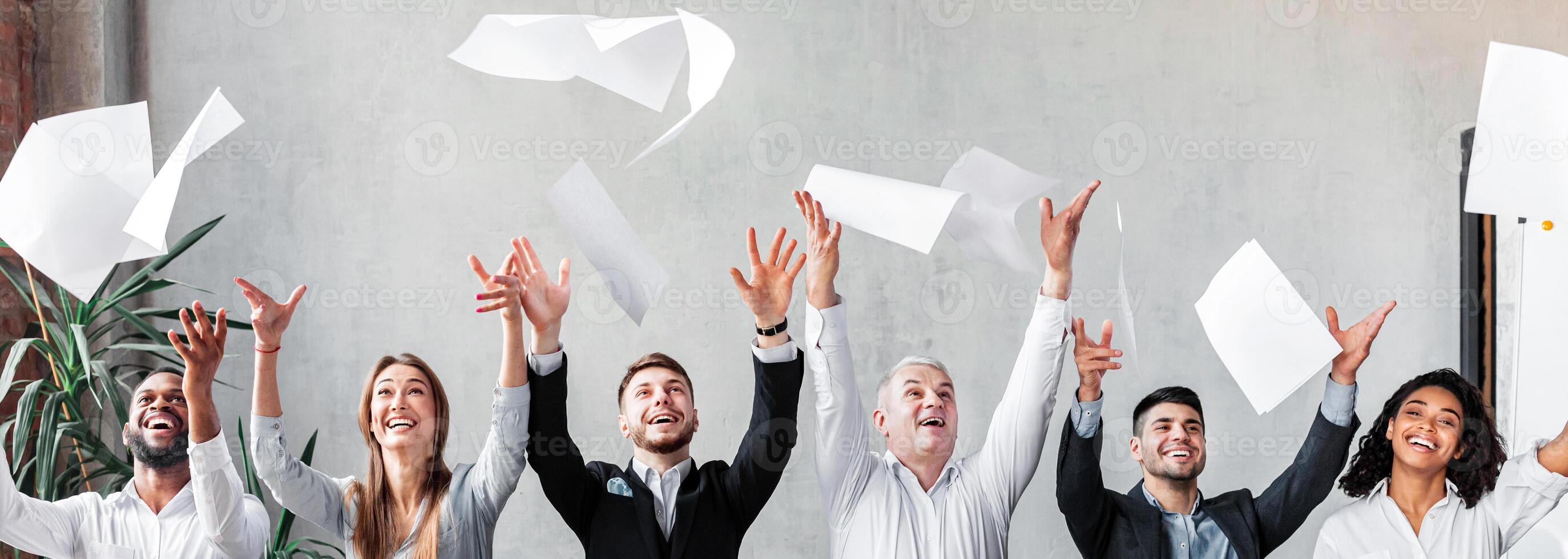 Happy Businessmen And Businesswomen Colleagues Throwing Papers Celebrating Business Success Sitting At One Table In Modern Office. Panorama photo