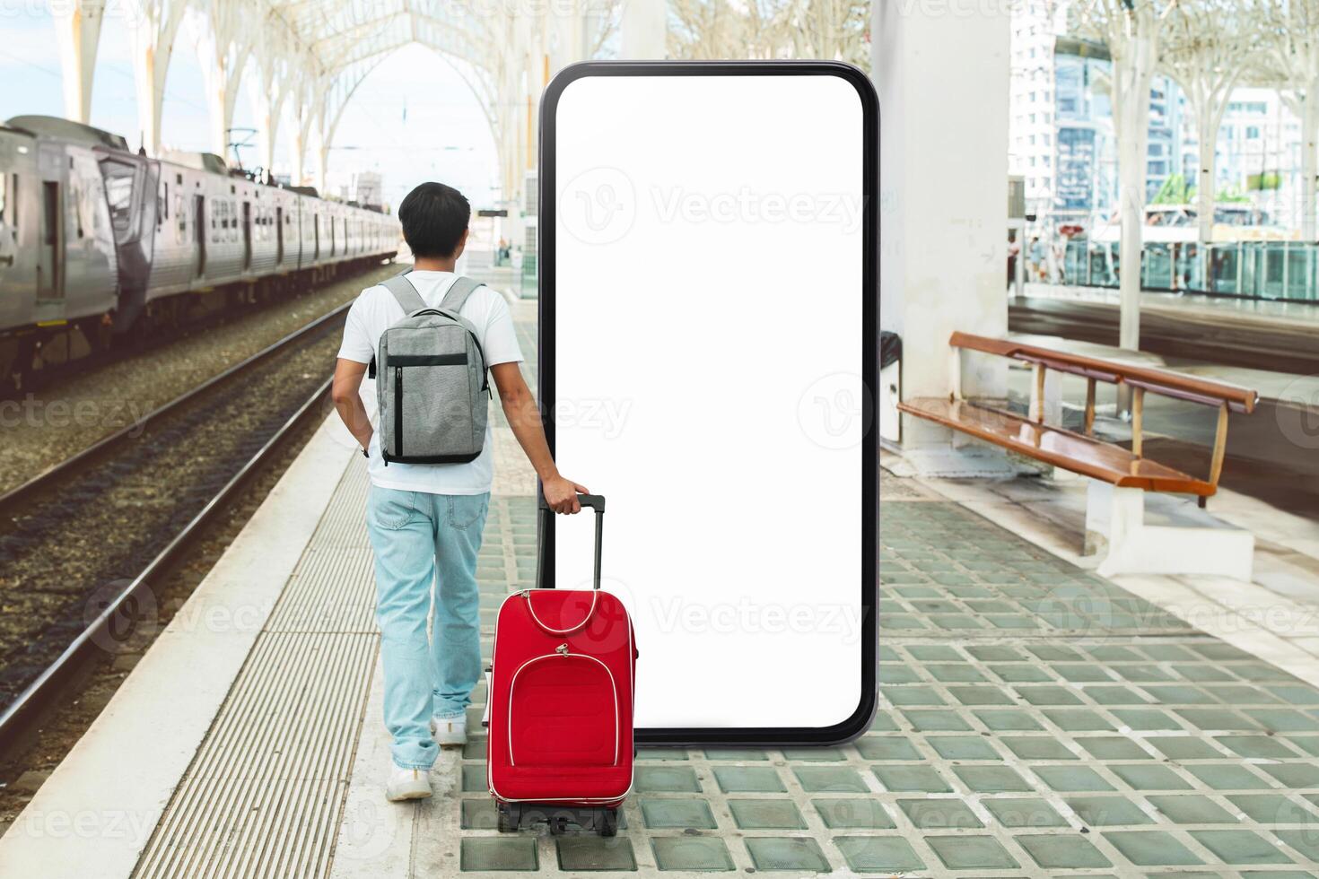 A person stands at a train station, pulling a red suitcase. They gaze at a large blank screen, possibly awaiting information about train schedules or advertisements. photo
