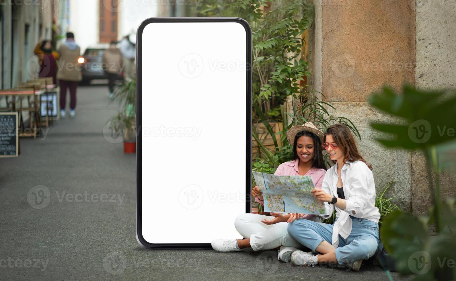 Two young women sit together in a lively alley, engrossed in a map. They are surrounded by greenery and a blank phone screen, indicating they are on an urban adventure. photo