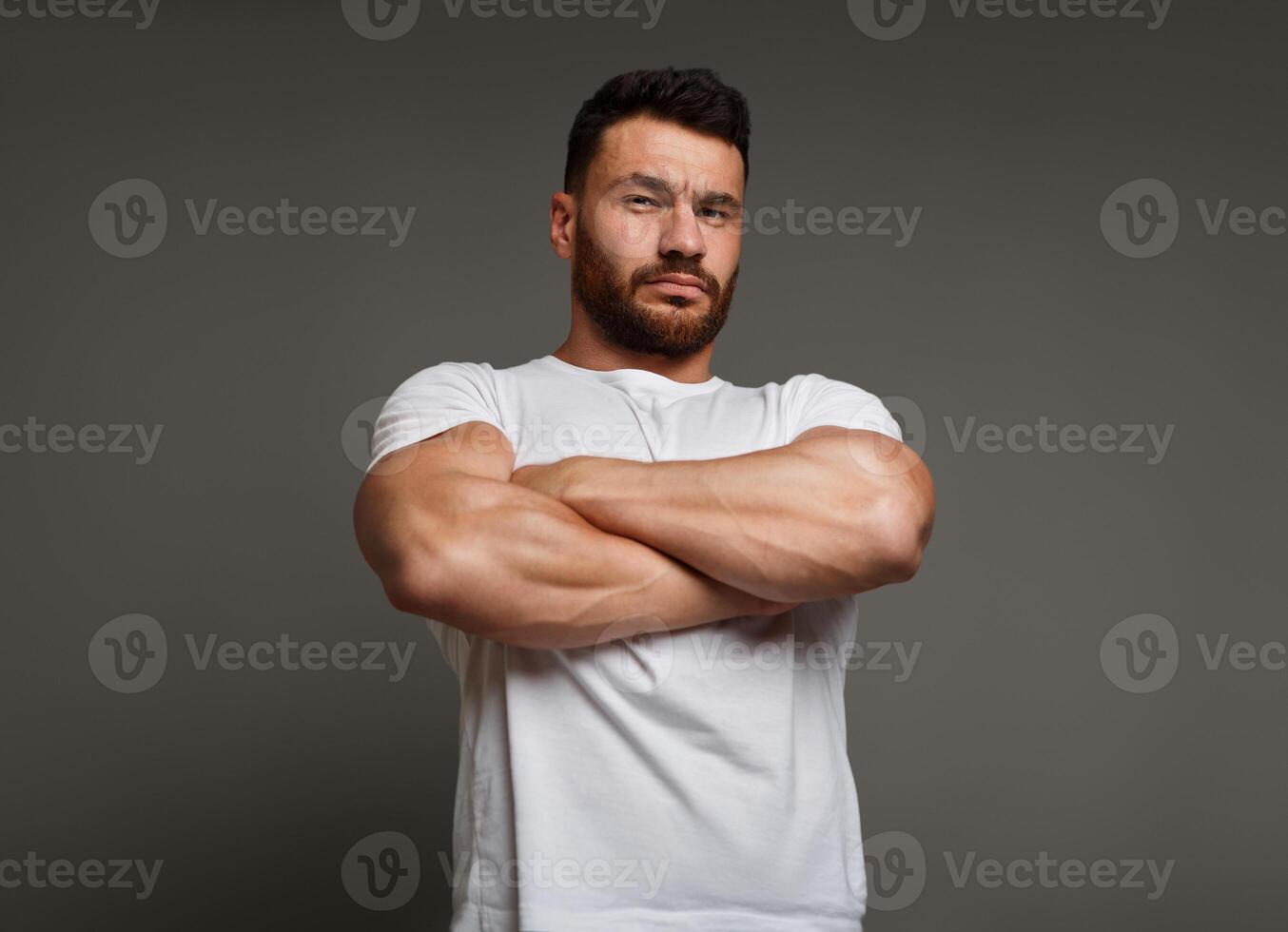 Muscle concept - suspicious young man with crossed big muscular arms showing his arrogant strength and male power, looking down at camera photo