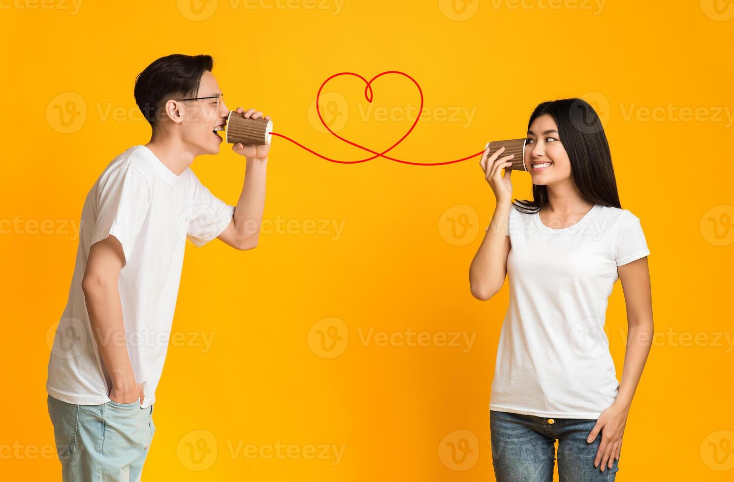 Asian guy telling his girlfriend about love, using can phone, orange background photo