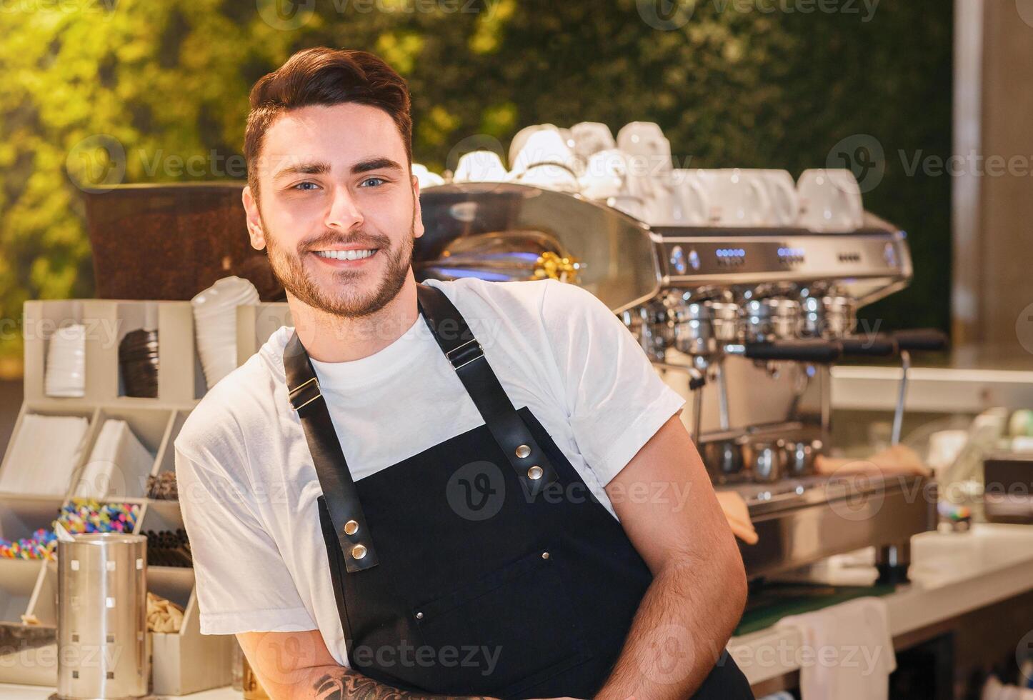 Barista Career. Cheerful Coffeemaker Guy In Uniform Posing Near Coffee-Machine Standing In Cafe photo