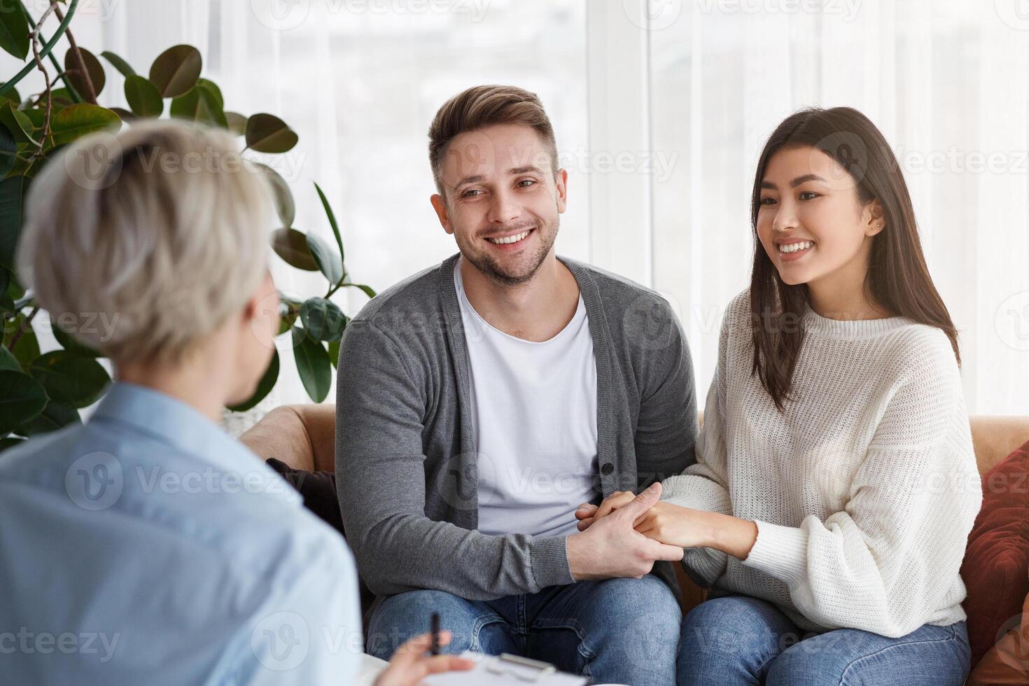 Reconciliation. Smiling Multiethnic Spouses Holding Hands Reconciling After Quarrel Sitting In Family Psychotherapist's Office photo