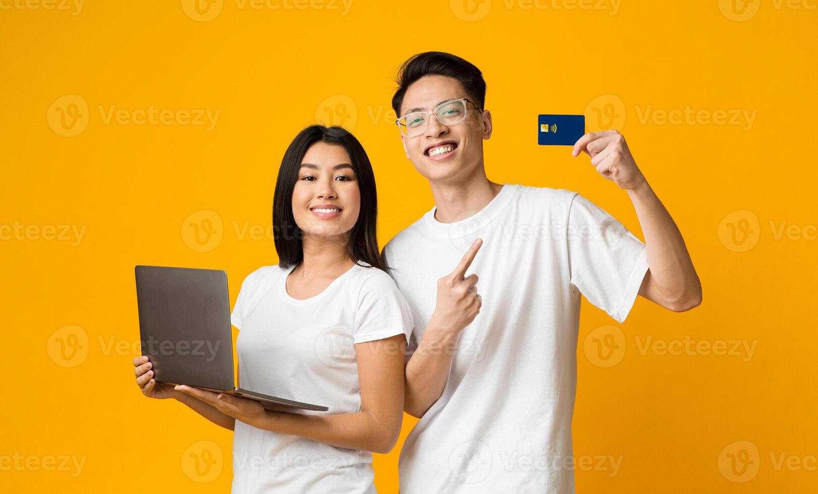 Positive asian couple recommending credit card for shopping, ecommerce concept, yellow background photo