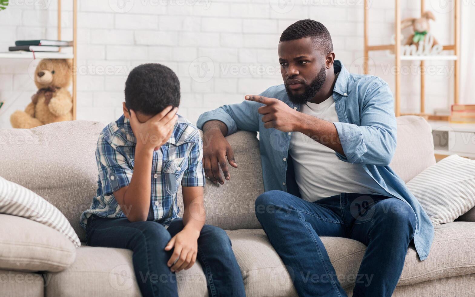 Angry black father scolding stubborn little son for bad behavior at home, boy making facepalm gesture, free space photo