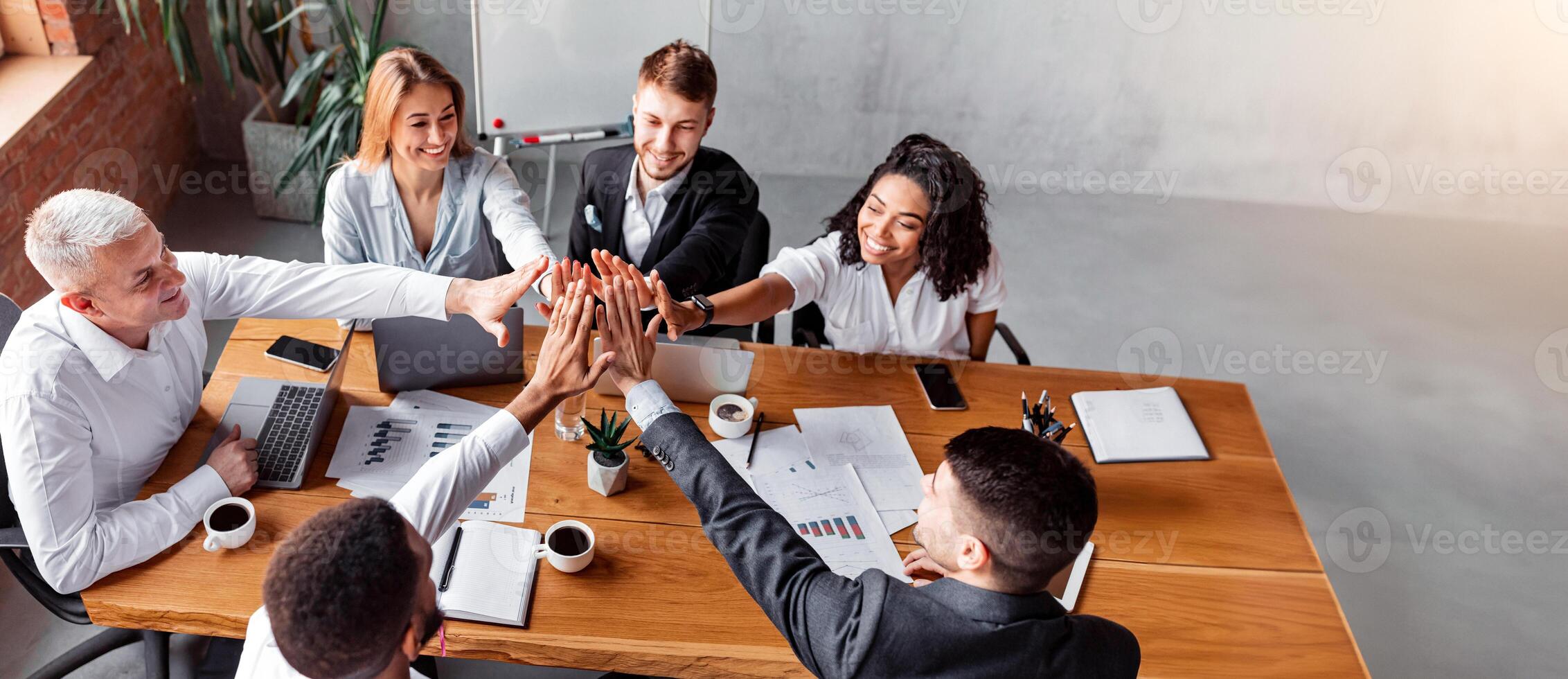 Corporate Spirit. Happy Business Team Giving High-Five Celebrating Success At Work Sitting At Desk In Modern Office. High Angle photo