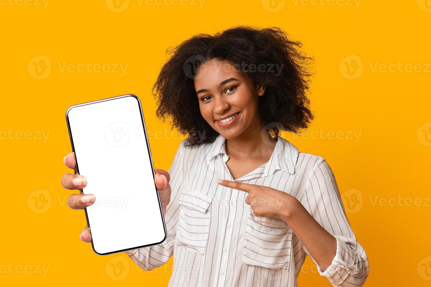 Check This App. Smiling Black Woman Holding And Pointing At Digital Tablet With Black Blank Screen, Posing Over Yellow Background, Empty Space photo