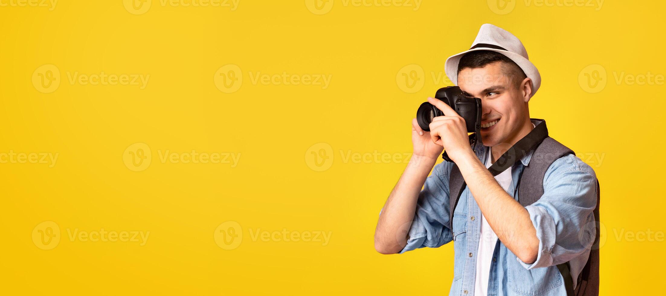 Active traveler happy young guy taking photos, using camera over orange background, panorama with copy space photo