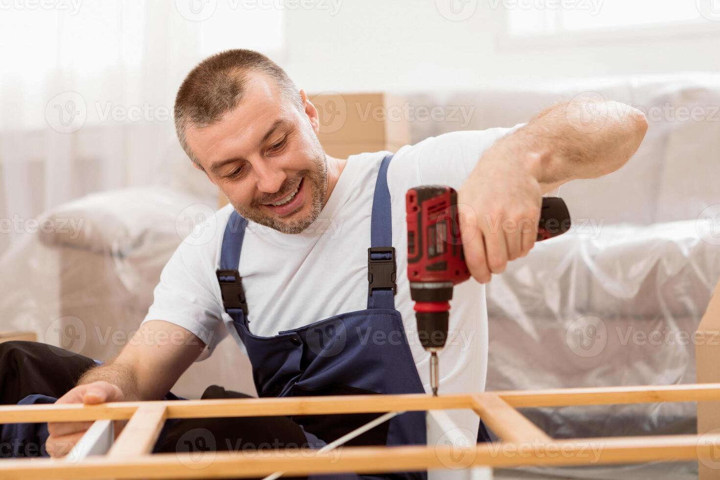 Happy Craftsman Working Using Drill Tool Fixing Wooden Cabinet Sitting On Floor At Home. Professional Carpenter Repairing Furniture In Studio. Furnishing House Services, Carpentry Occupation. photo