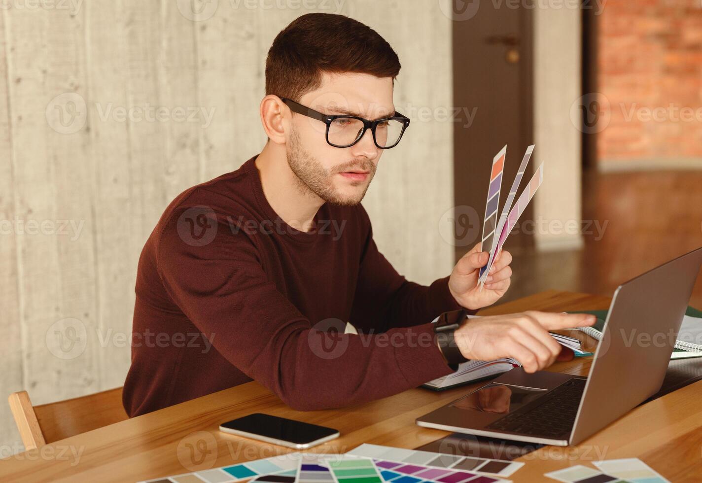 Designer At Work. Freelancer Guy Working On Laptop Choosing Color Samples Sitting In Modern Office. Selective Focus photo