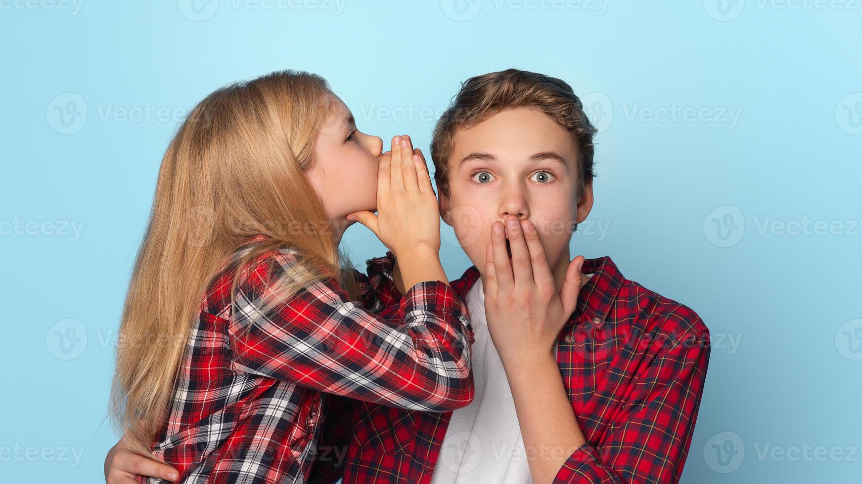 Cute Little Sister Sharing Secret With Her Teen Brother, Standing Together On Blue Background With Free Space photo