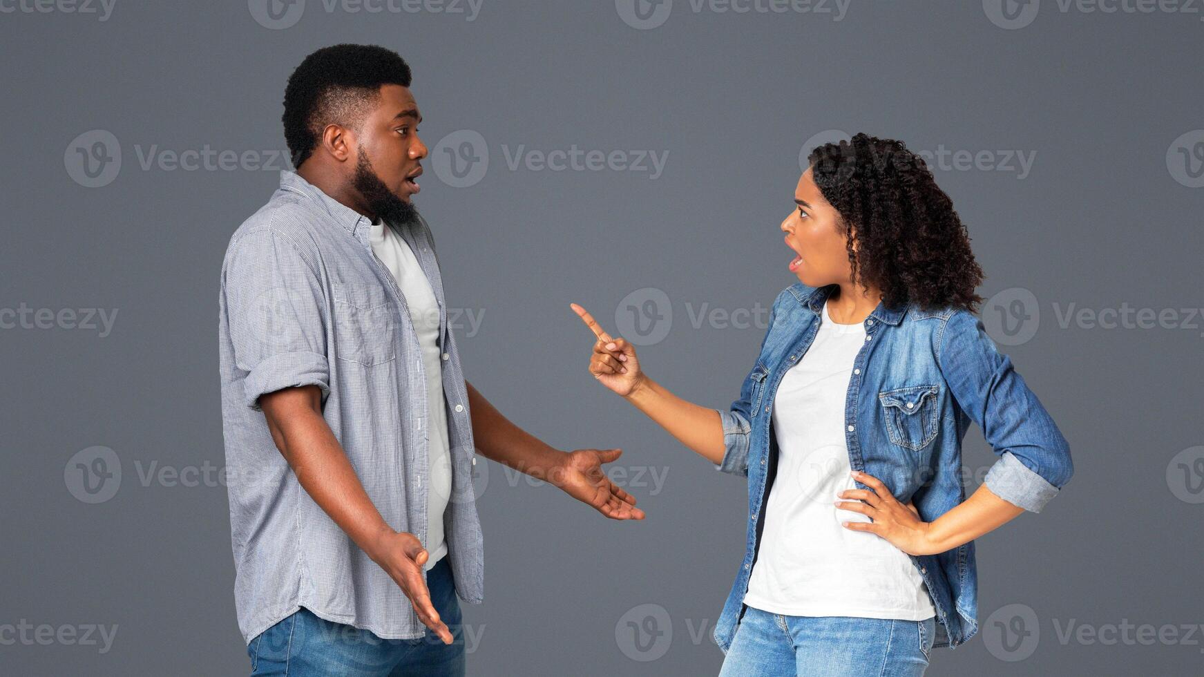 Misunderstanding in relationship. Furious black woman blaming her boyfriend, standing together over light background with free space photo