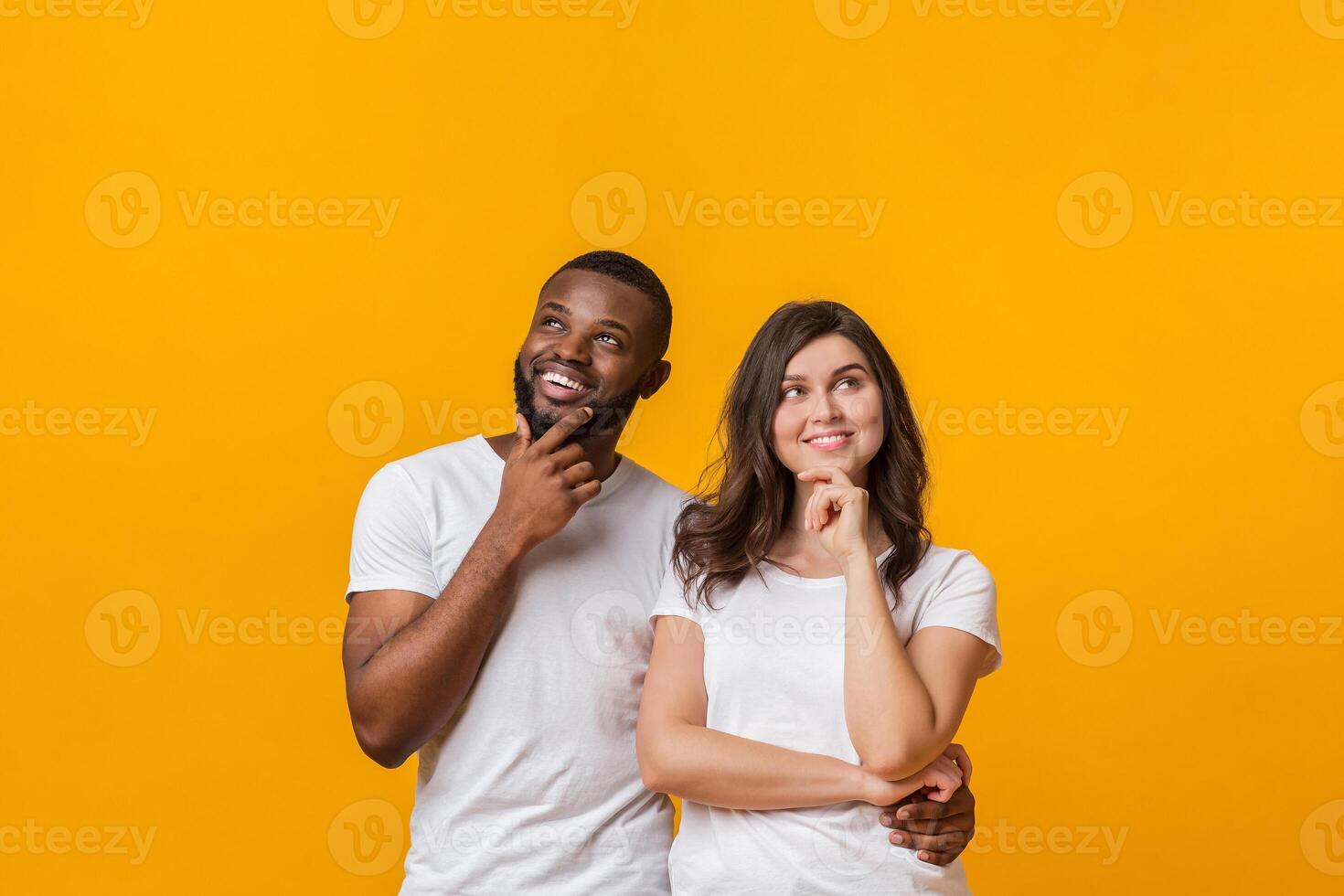 Portrait of pensive young interracial couple thinking about something and looking away upwards over yellow background with empty space photo