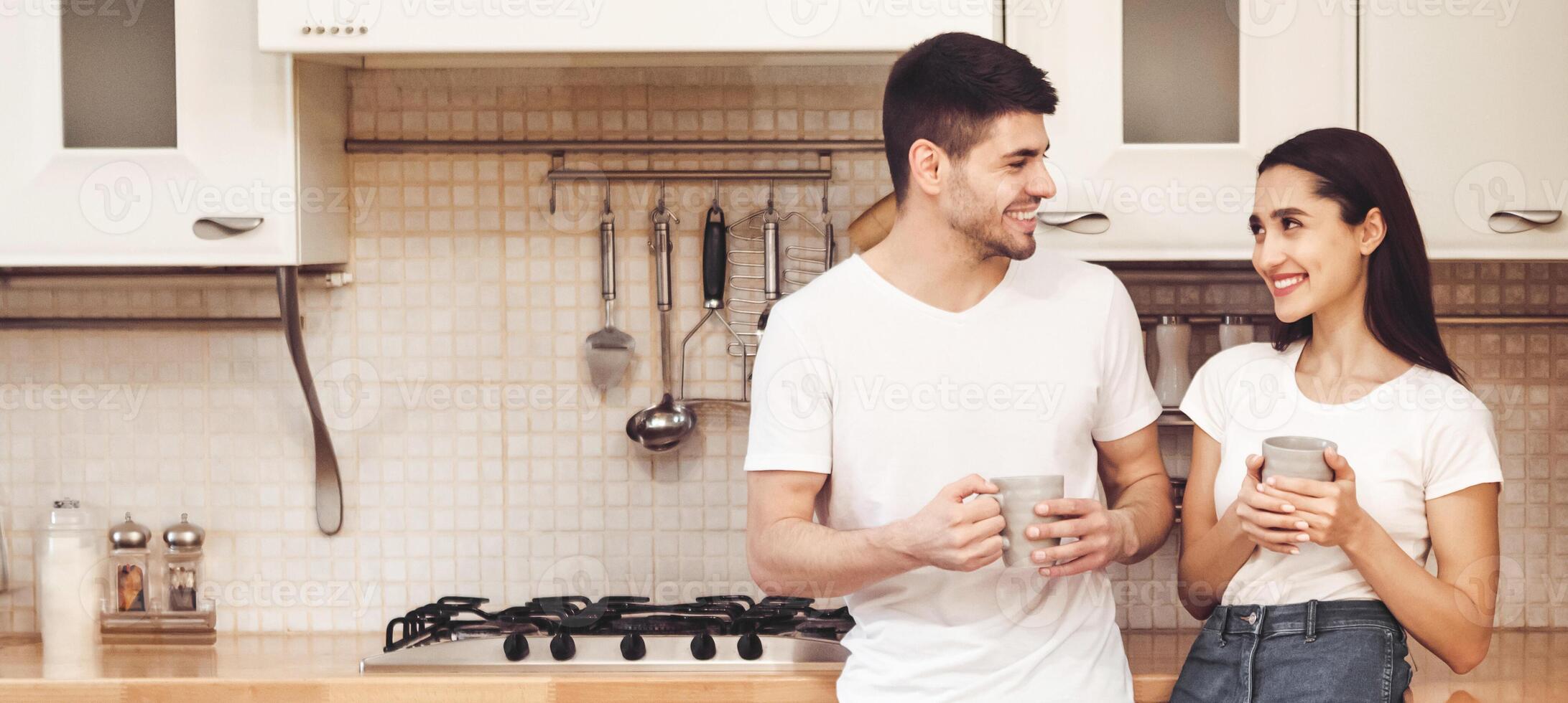 Spending Time Together. Full length portrait of cute young man and woman drinking coffee standing in modern kitchen photo