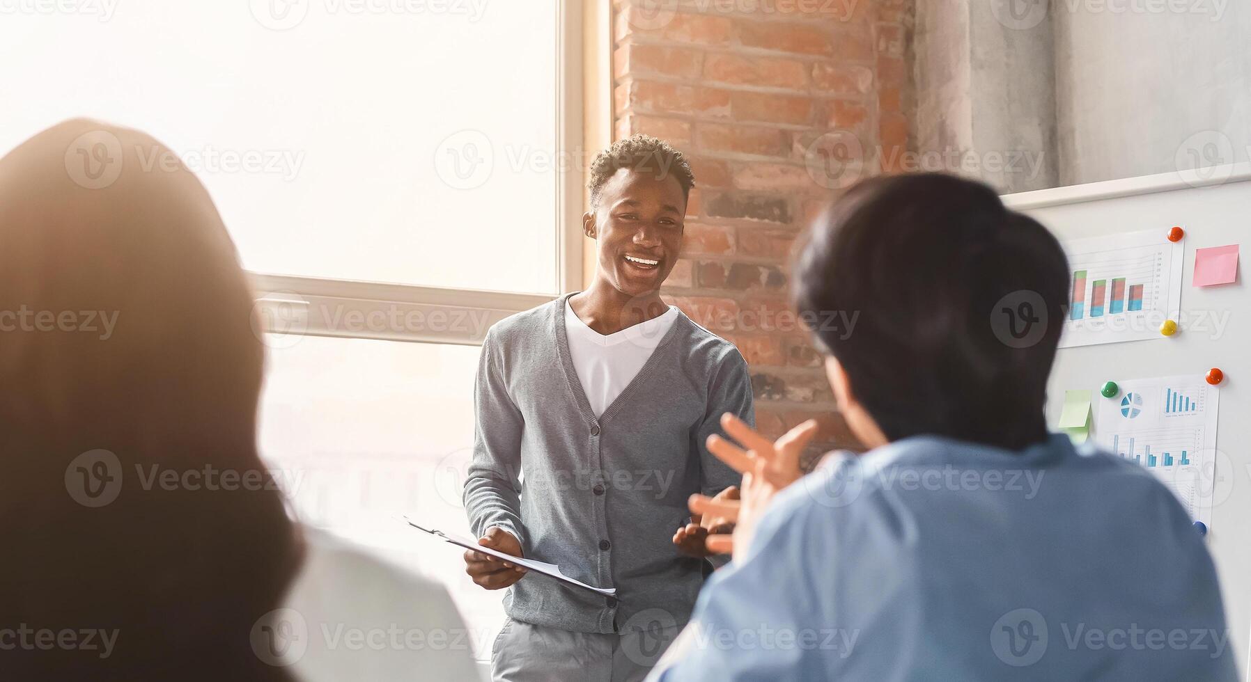 Cheerful black employee talking to colleagues while business presentation, office interior photo