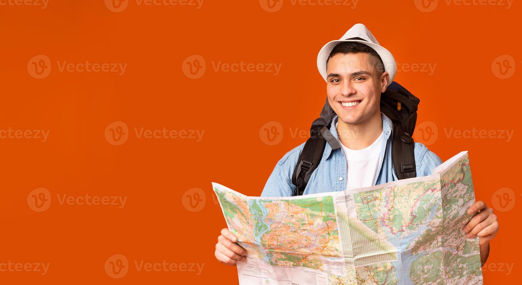 Joyful hiker with big backpack holding map over orange studio background photo