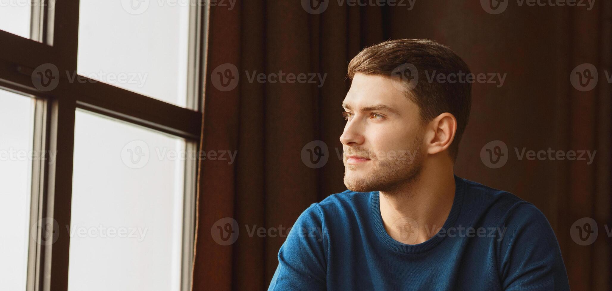Millennial Guy Portrait. Confident Young Man Looking Aside Sitting Near Window In Modern Loft Interior Indoor. Copy Space photo