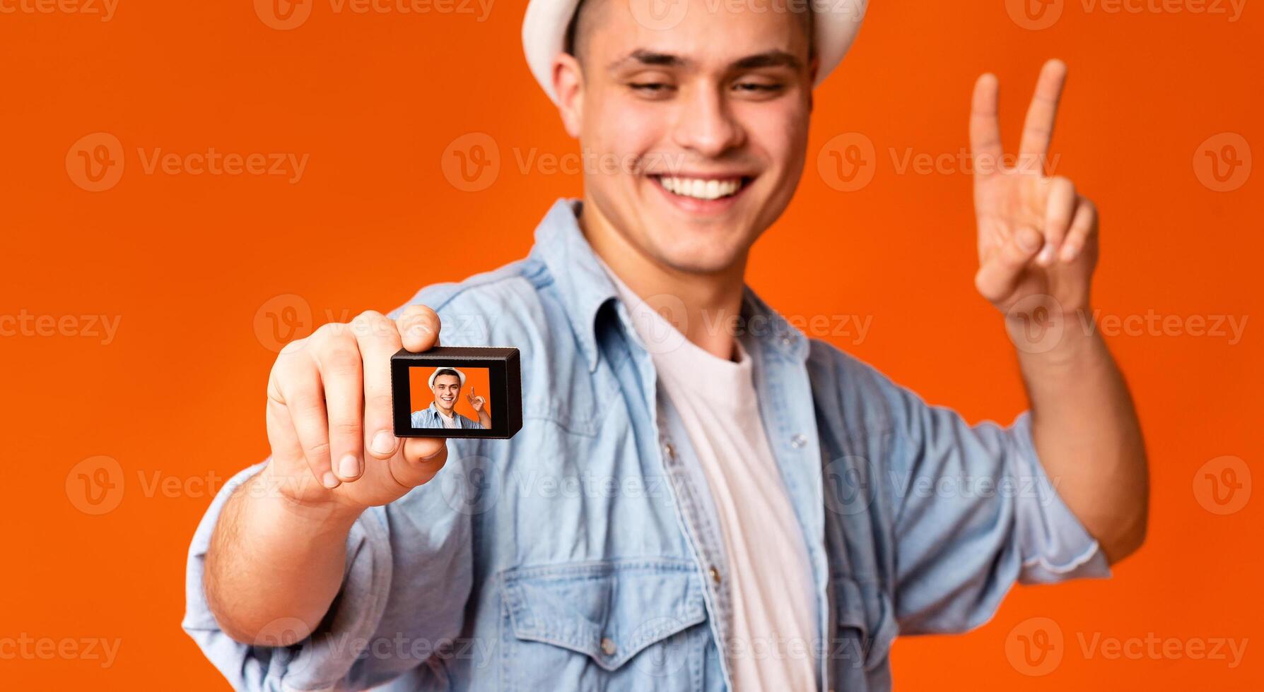 Happy handsome guy tourist posing and using action camera over orange studio background photo