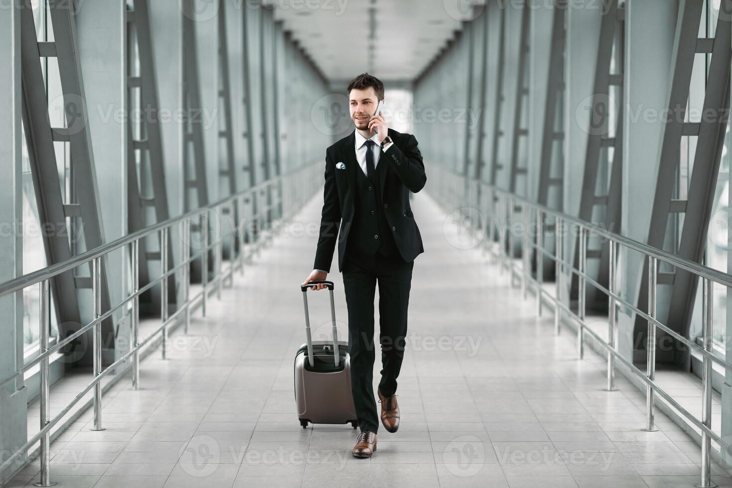 Urban business man in suit talking on smart phone traveling walking with luggage inside the airport, empty space photo